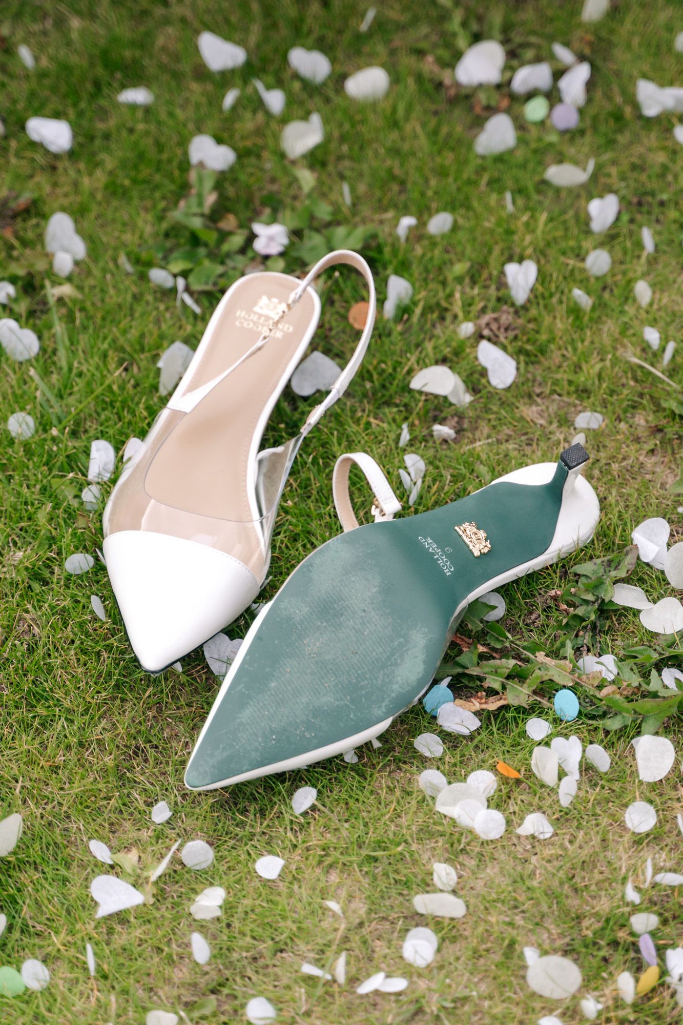 Elegant mint green and white bridal shoes scattered on grass amongst white flower petals.
