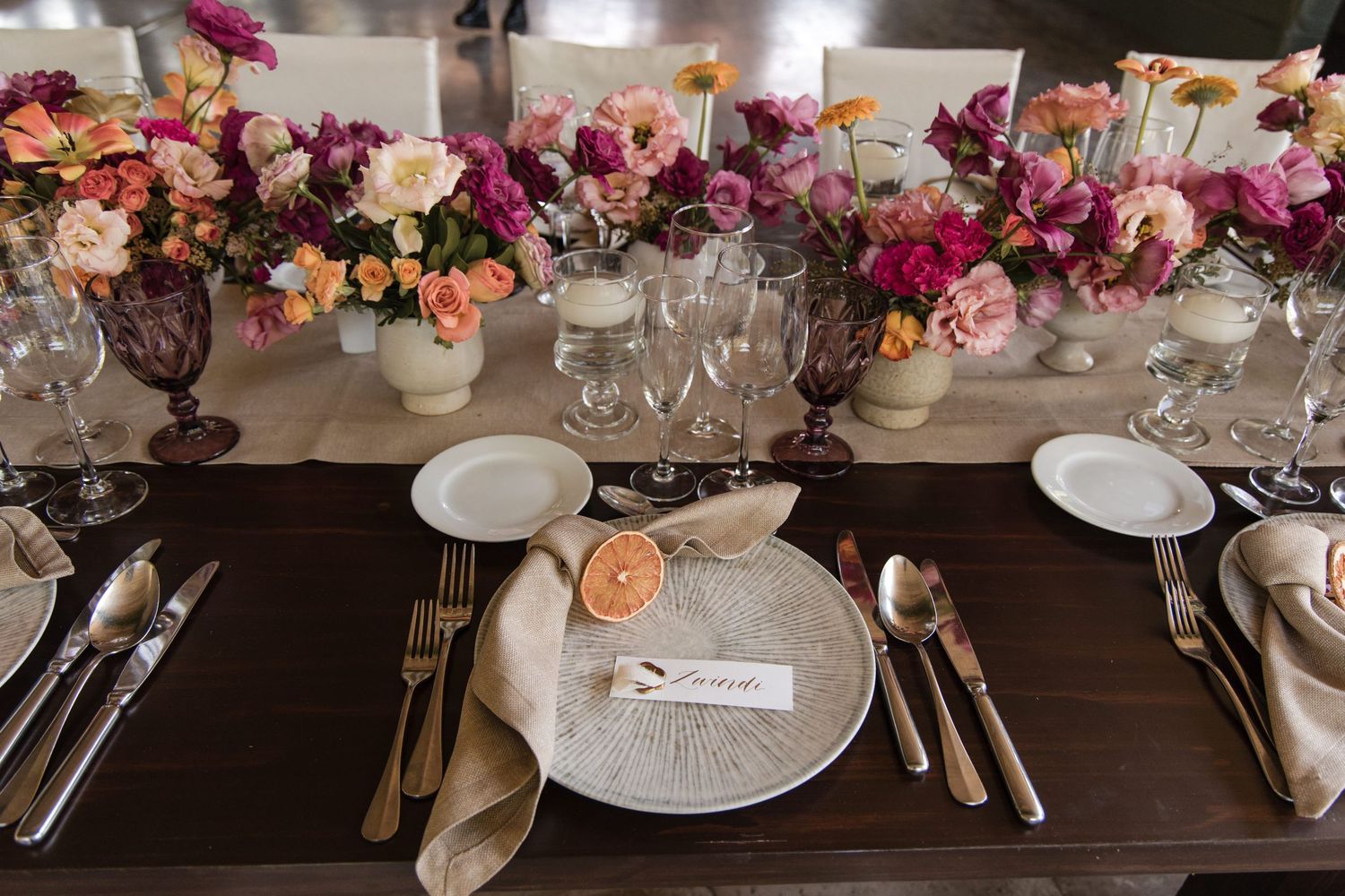 Elegant wedding table setting with vibrant pink and purple floral arrangements and fine dinnerware.