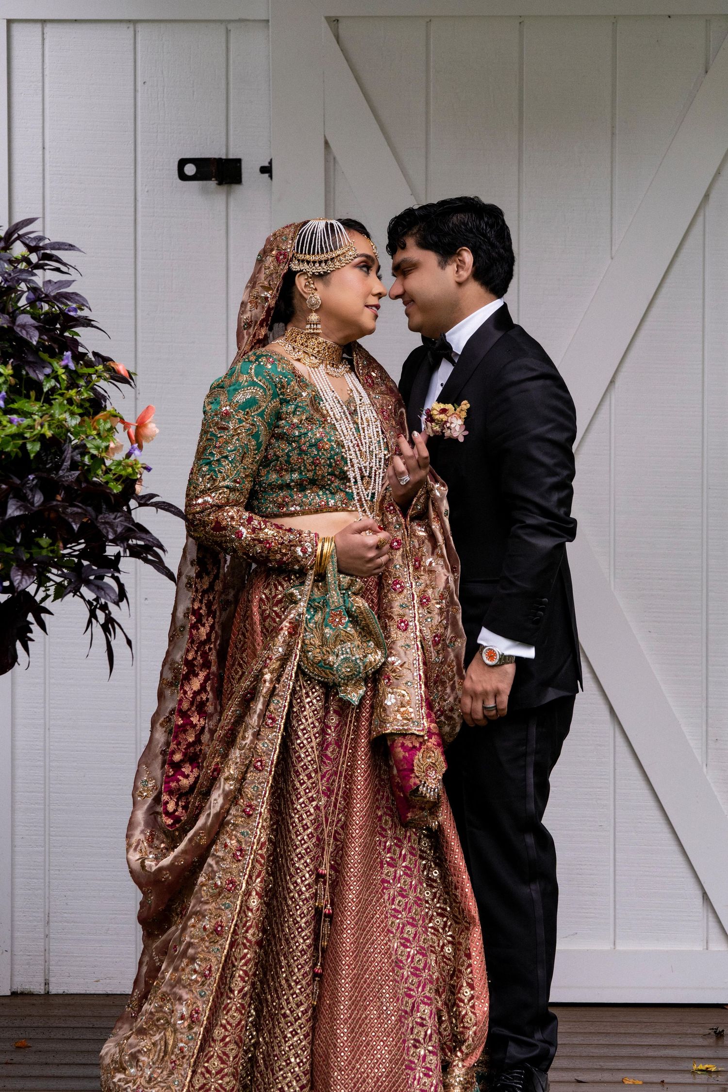 A couple in wedding attire share an intimate moment, with the bride wearing an ornate rose gold South Asian lehenga.