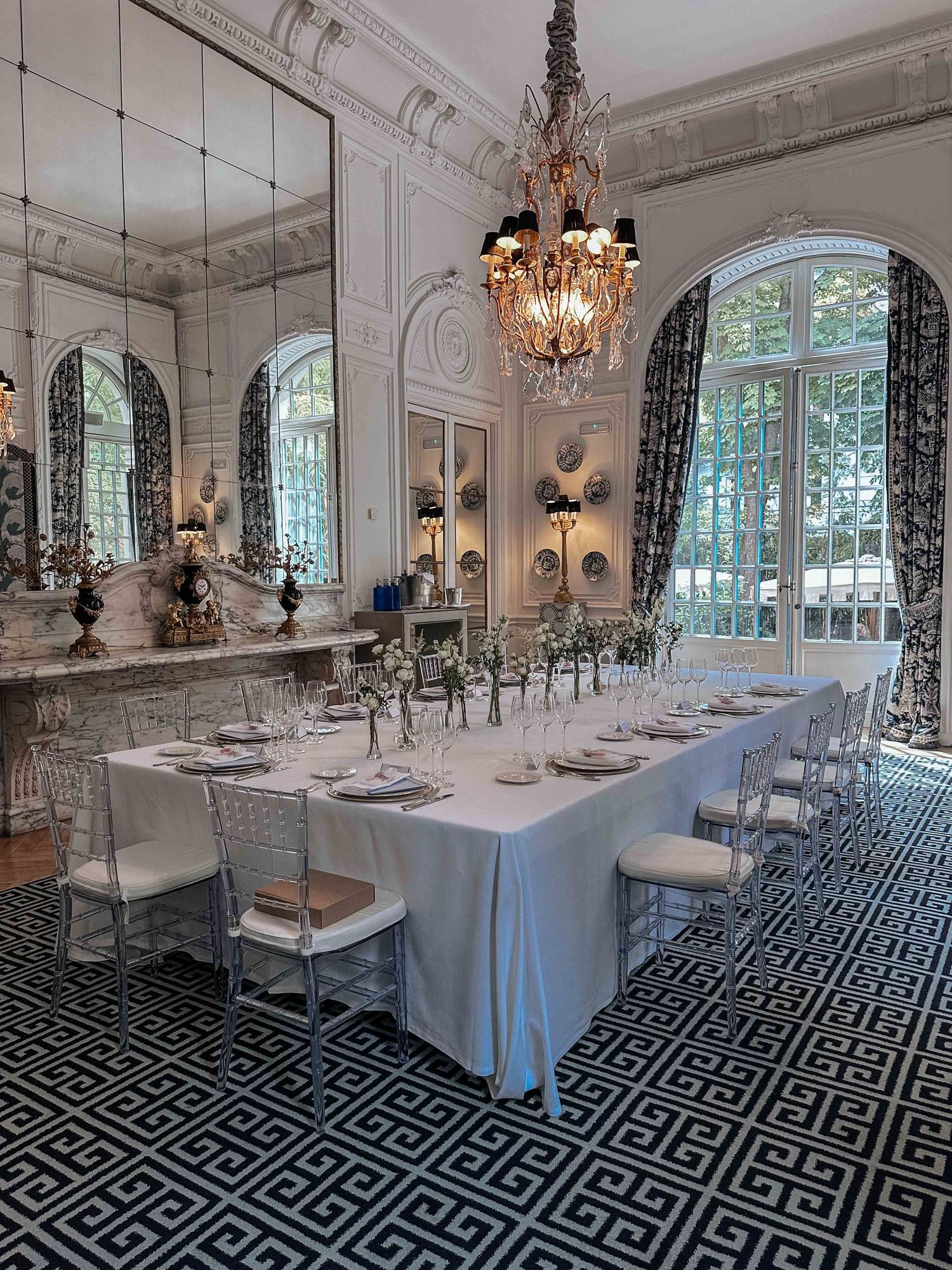 Elegant dining room with crystal chandelier, mirrored walls, arched windows, and geometric patterned floor in classic style.