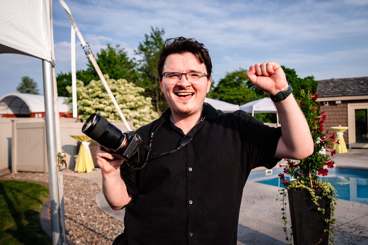 Person in black shirt celebrates joyfully outdoors on sunny day.