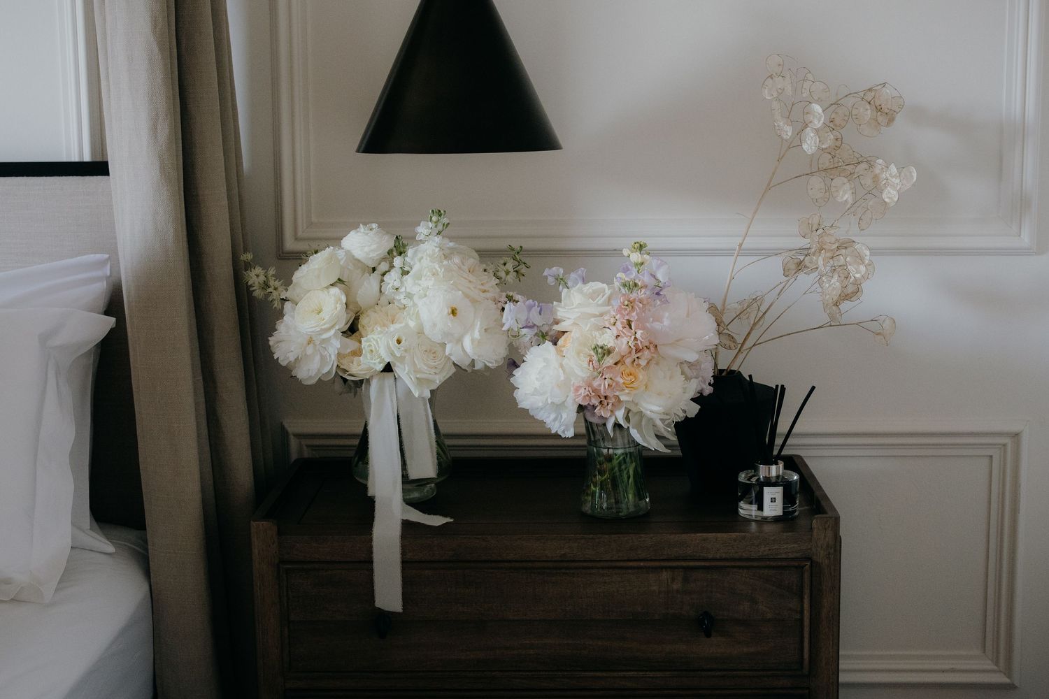 Elegant white and blush peony bouquets in glass vases on a dark wood nightstand with a black lamp at the old vicarage boutique hotel.
