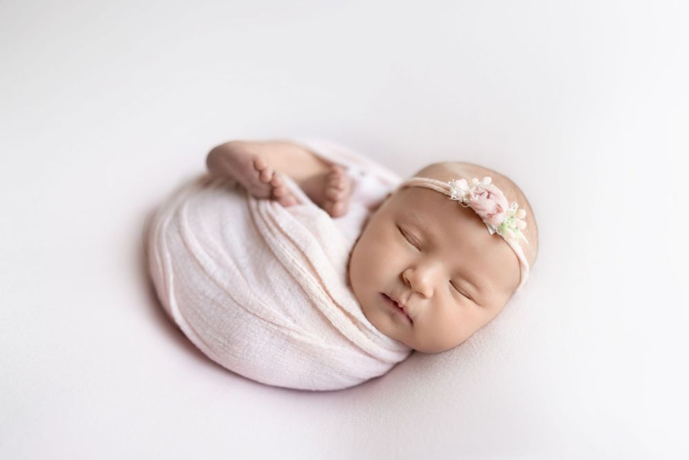A peaceful newborn baby in soft pink swaddle sleeps soundly during professional photography session.