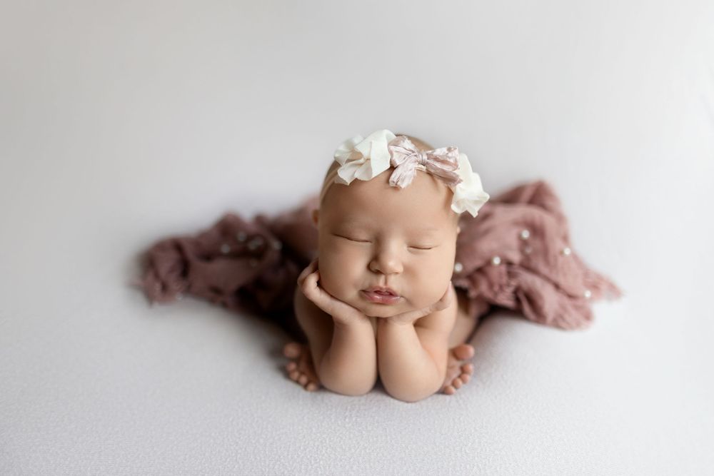 A newborn baby sleeping peacefully in soft pink and beige tones on a neutral backdrop.