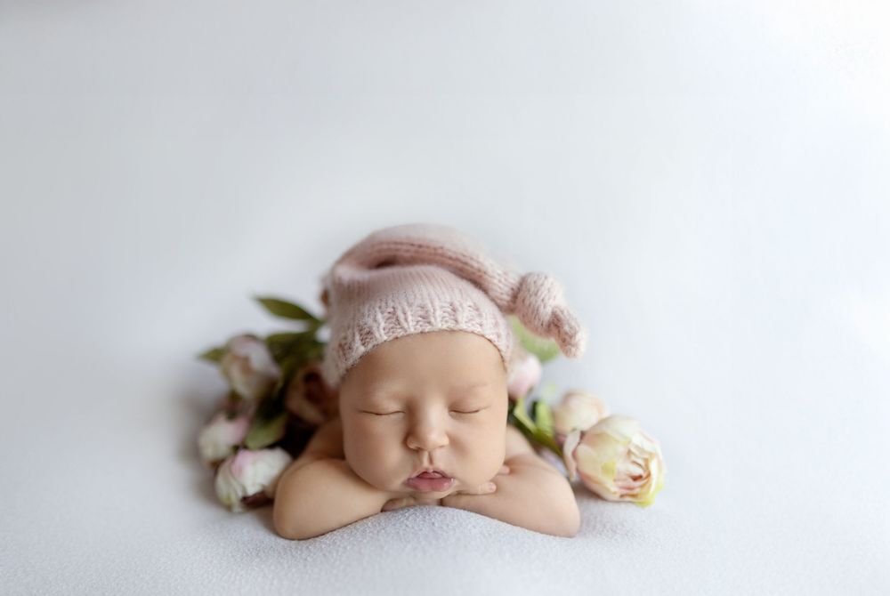 Sleeping newborn baby lying on white blanket surrounded by delicate pink and cream roses.