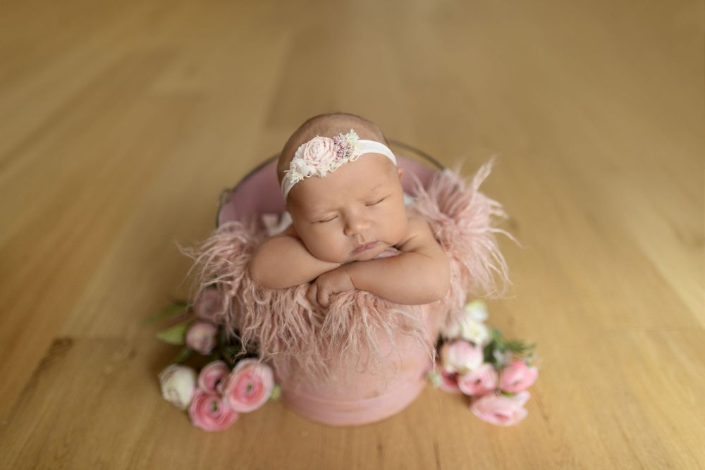 Newborn baby sleeping peacefully in pink wrapping with delicate floral decorations on wooden floor.