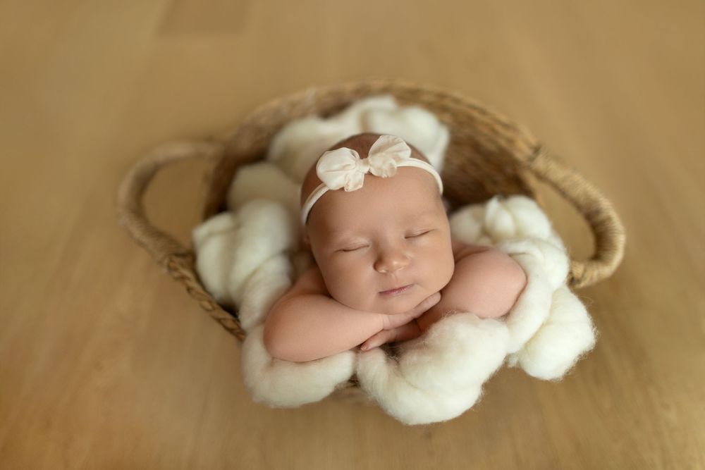 Sleeping baby wrapped in soft white blankets on beige backdrop during professional newborn photography session.