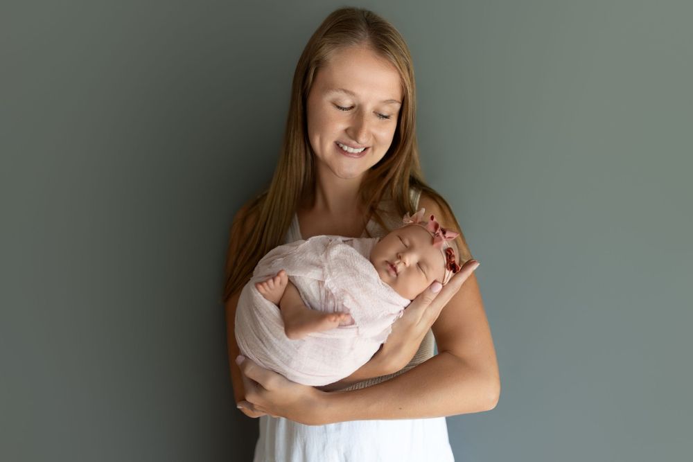 A tender moment between parent and newborn baby wrapped in white against a gray background.