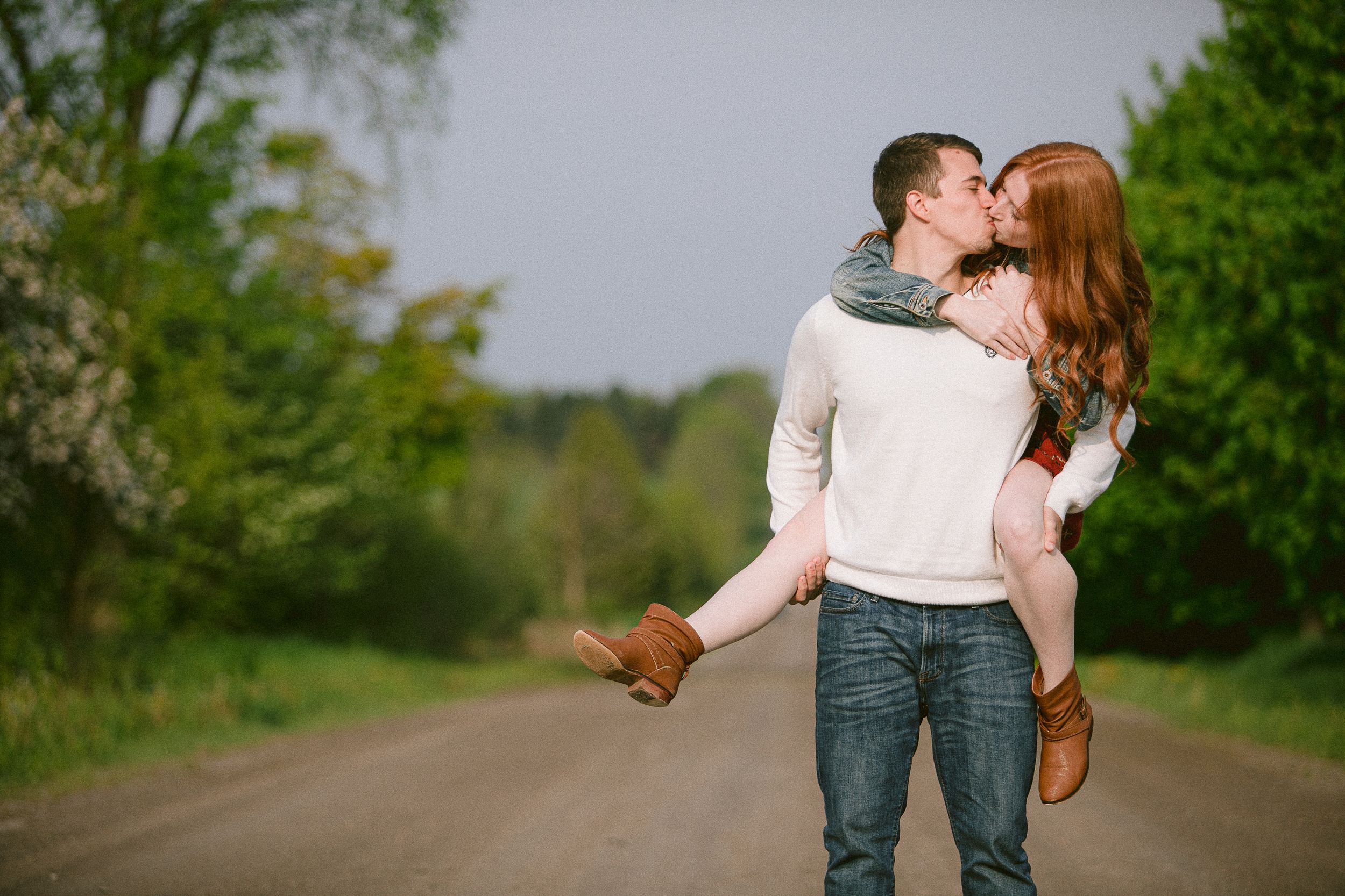 A couple shares romantic moments together on a tree-lined path during an outdoor photo session.