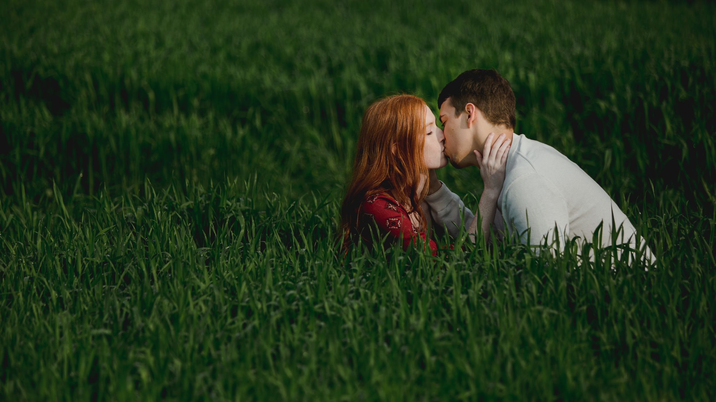 A couple shares a romantic moment while lying in a lush green meadow on a sunny day.