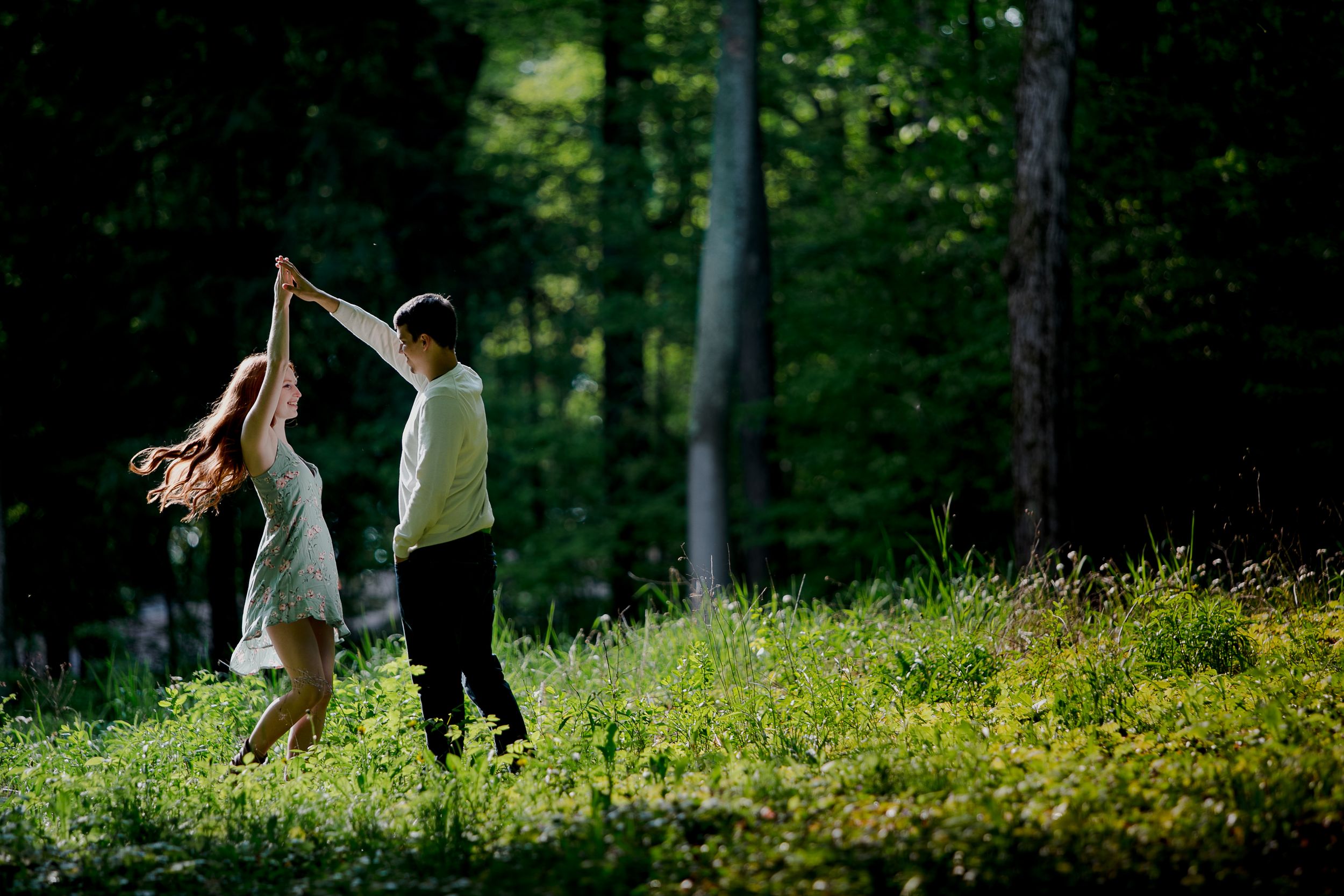 Two people stand together in a meadow filled with yellow wildflowers and surrounded by forest.