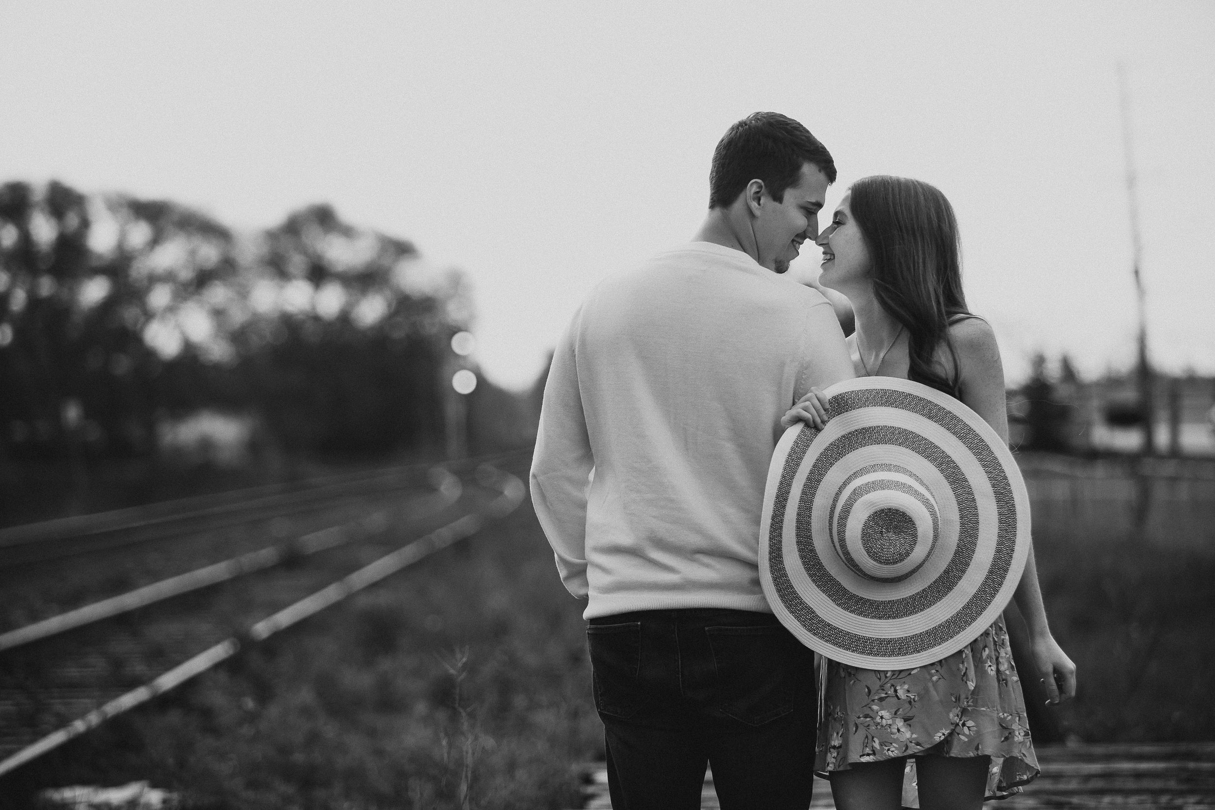 A couple shares an intimate moment together while walking along railroad tracks at sunset.