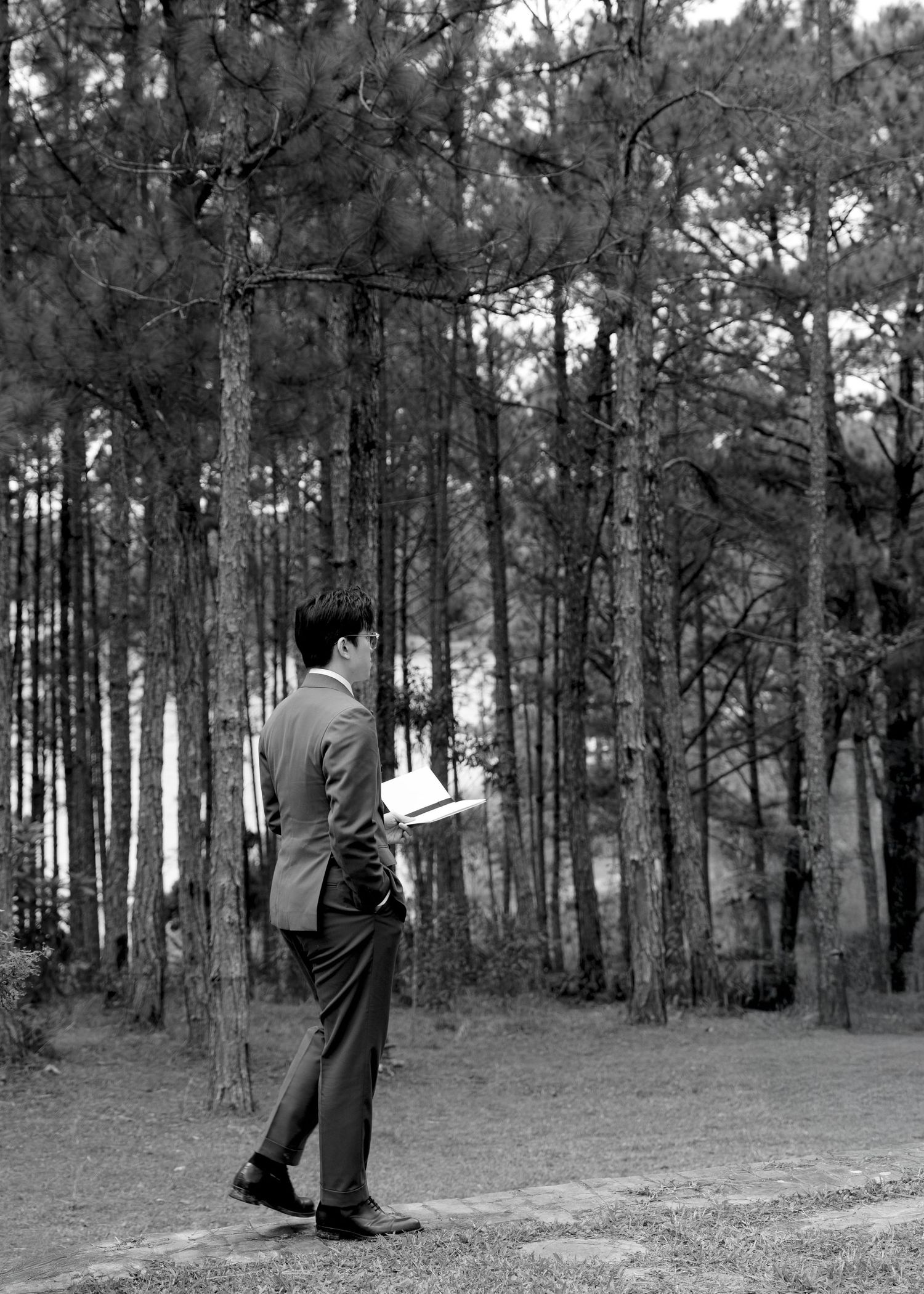 Black and white photo of groom reading vows in a pine forest setting.
