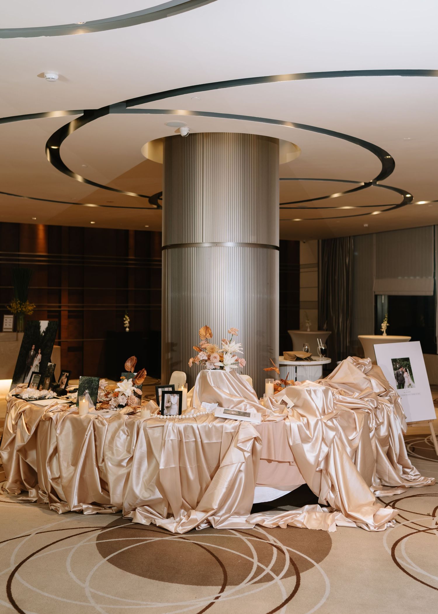 Elegant wedding reception lobby with champagne satin draped tables surrounding a large decorative column.