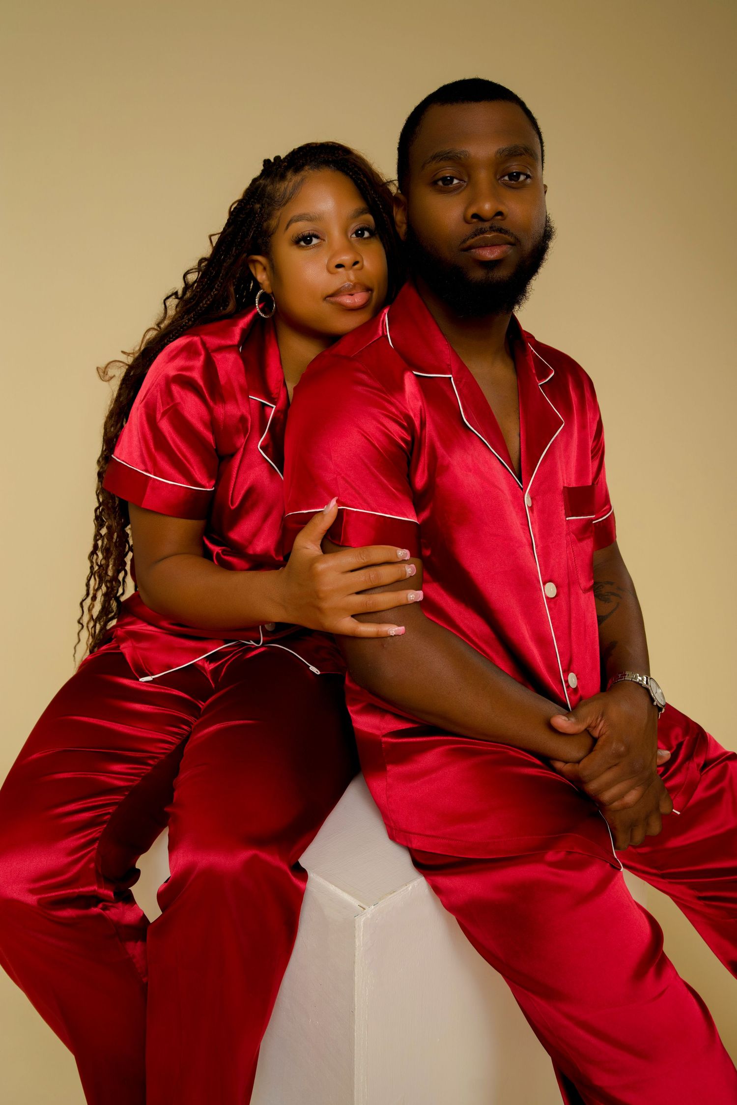 Couple in matching red silk pajamas embracing on white cube.