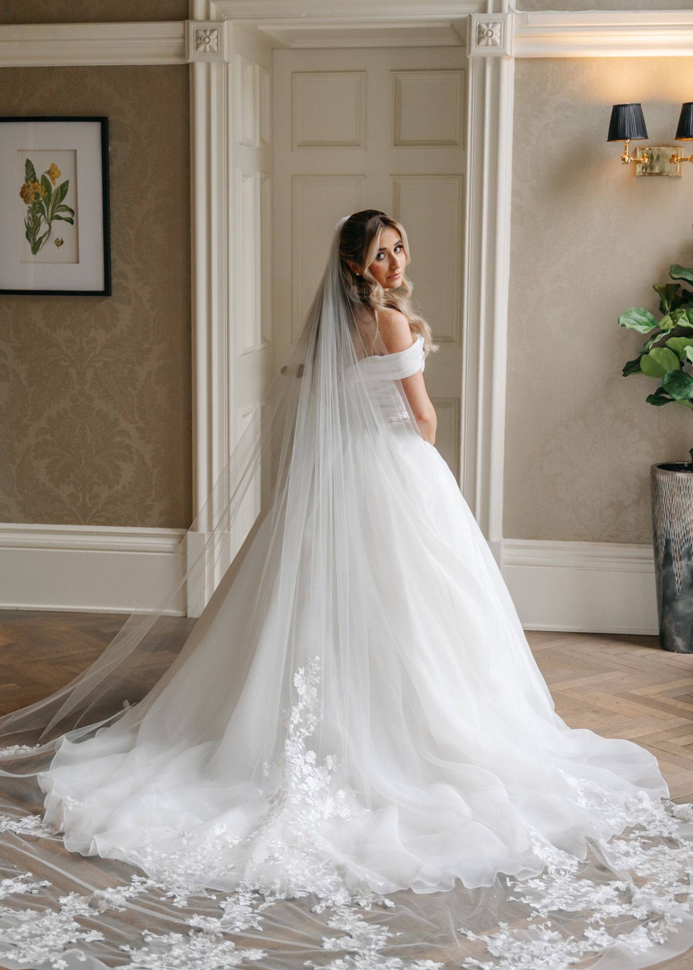 A bride in a flowing white gown with long train poses in an elegant interior setting.