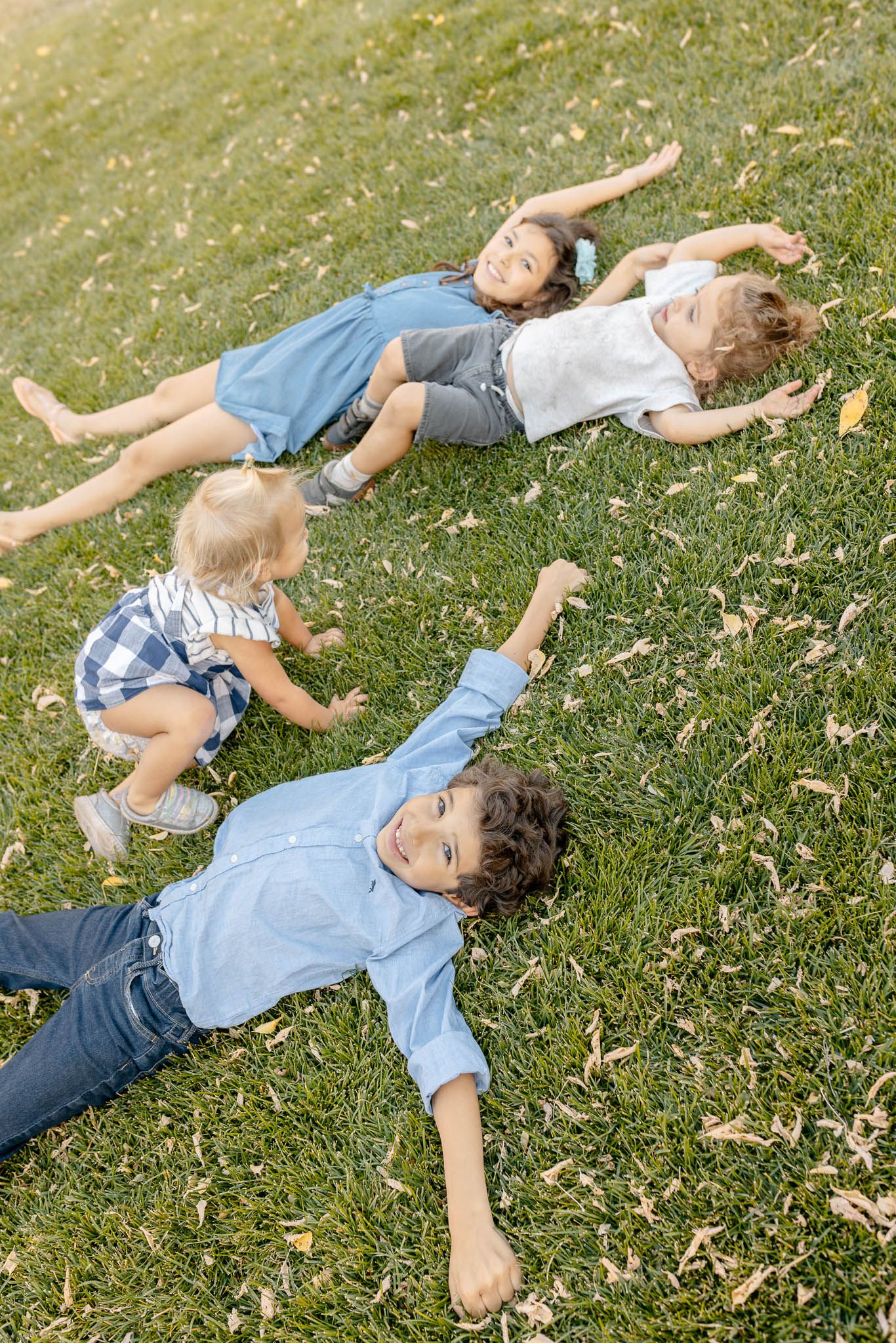 Two people lying in grass enjoying a playful and carefree summer moment in a park or backyard setting.