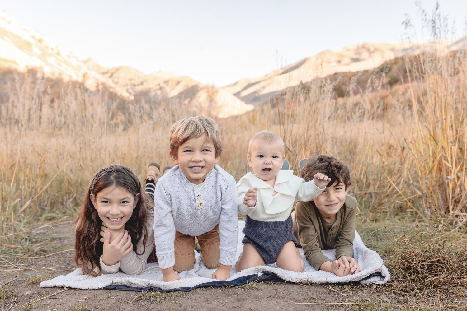 A family sits together on a blanket in a field surrounded by golden autumn grass at sunset.