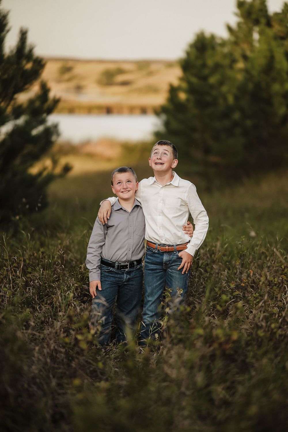 Two young children share a playful moment together while standing in a field of tall grass at sunset.