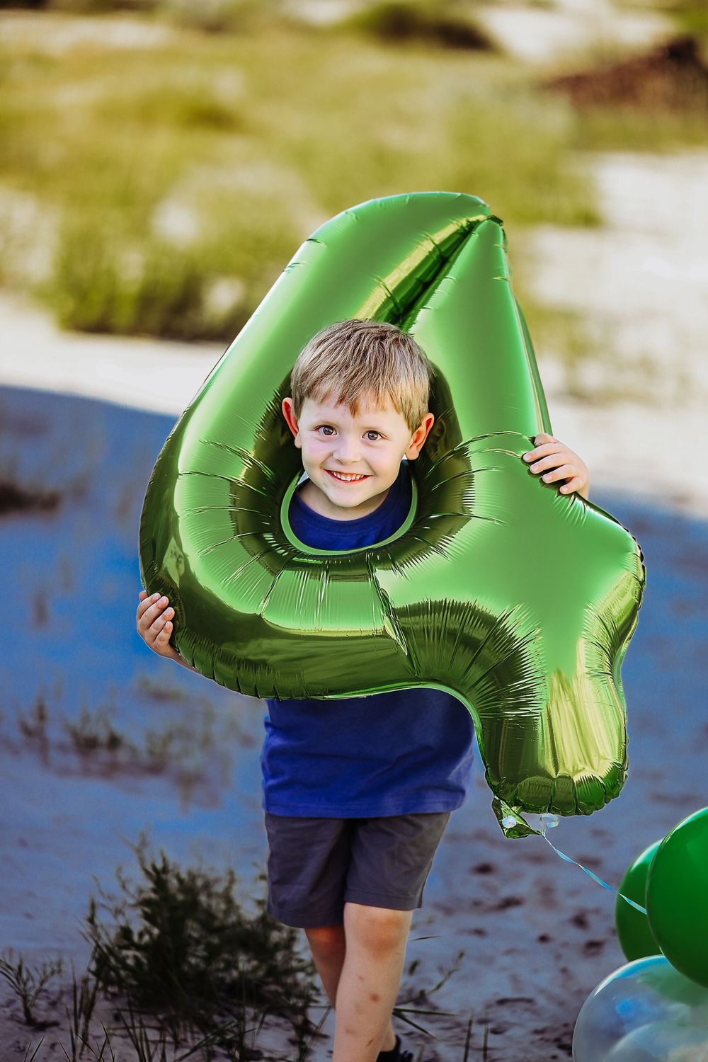 A child plays with a large green inflatable ring in shallow water on a sunny day.