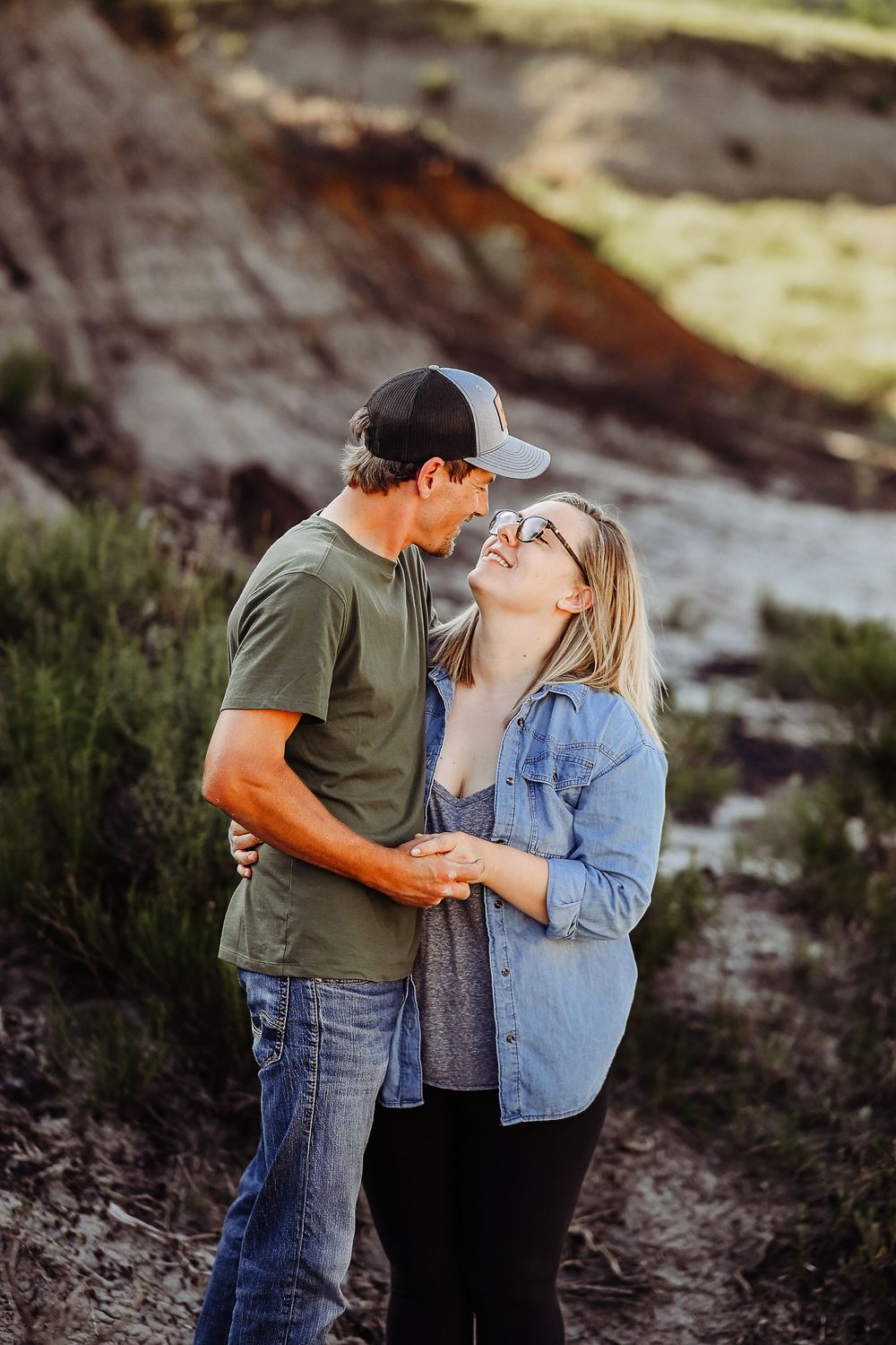 A couple shares tender moments together in a natural outdoor setting with rocky terrain and sunlit background.