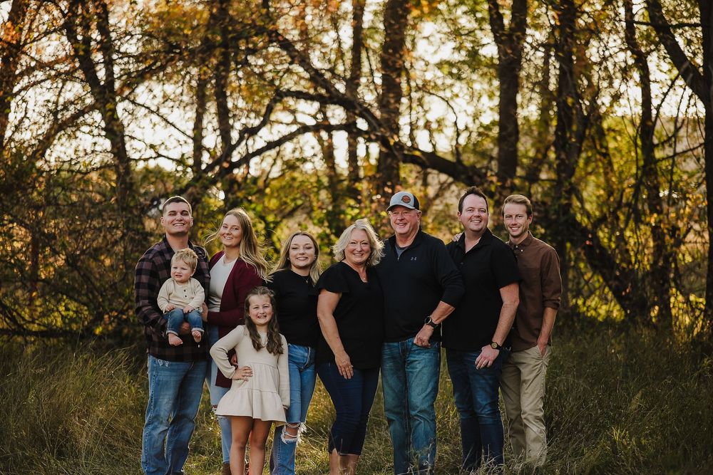 Multiple people pose together outdoors with trees and natural fall foliage in the background.