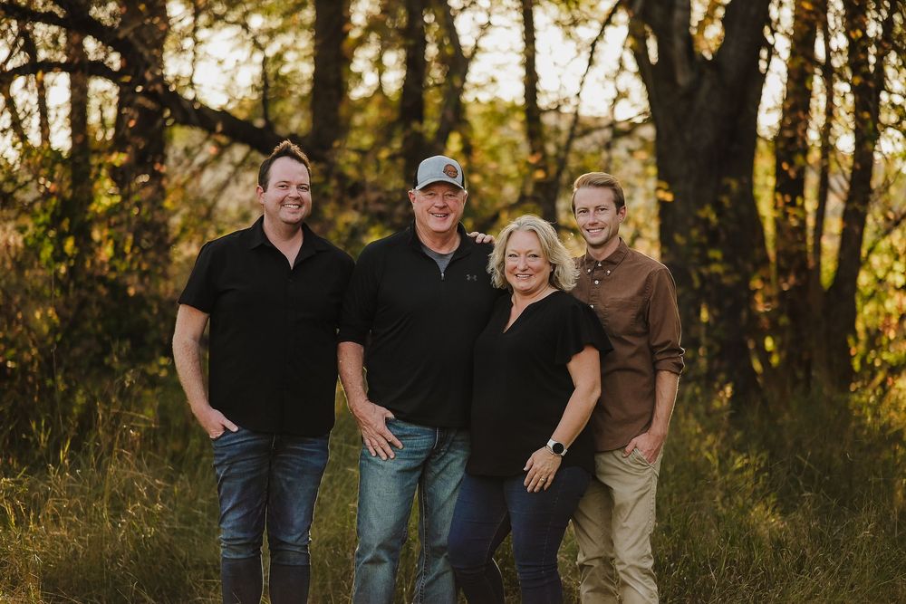 Family poses together outdoors during golden hour autumn photoshoot with sunlit trees in background.