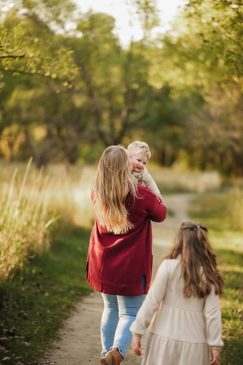 Two people walking together on a nature path surrounded by golden sunlit foliage.