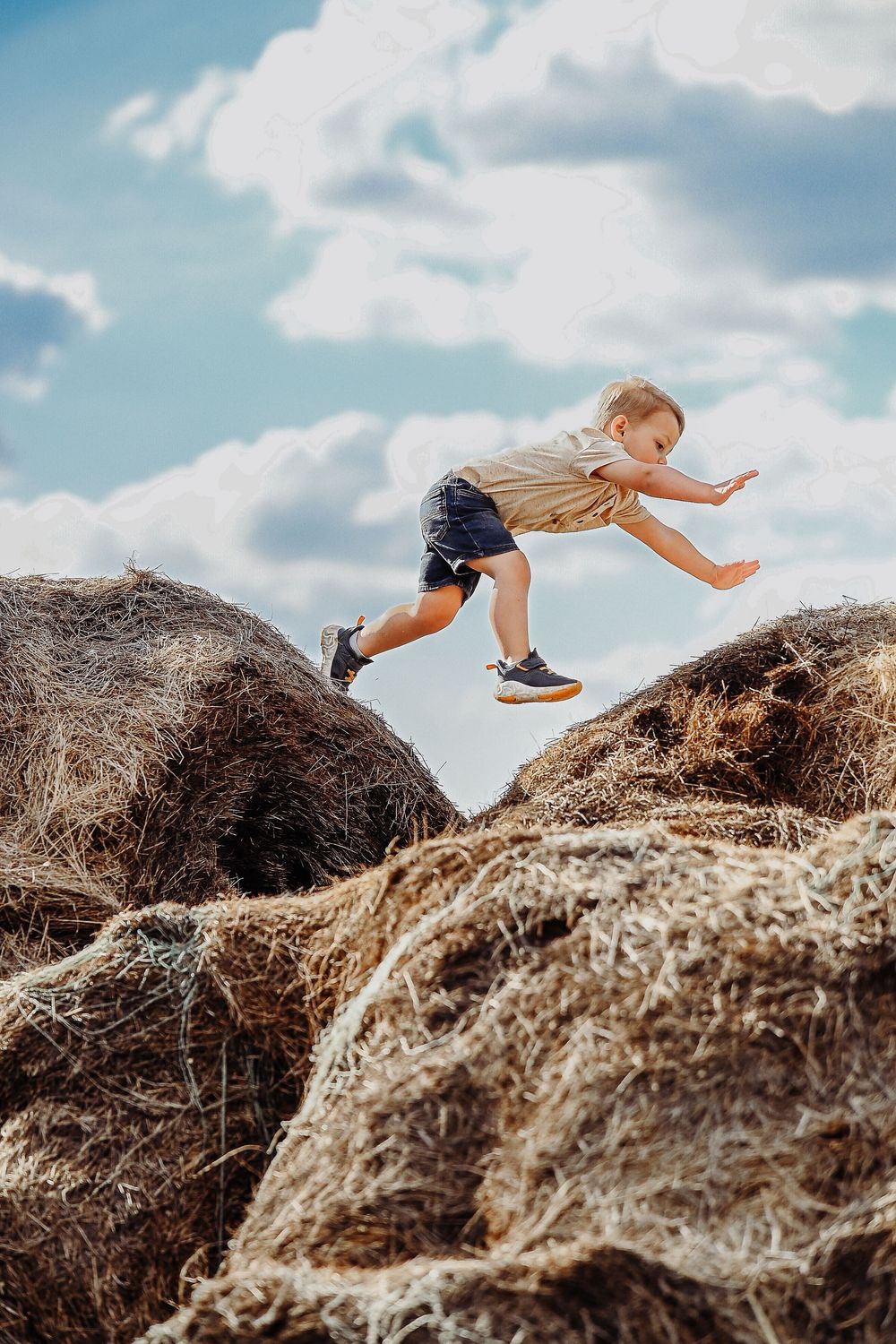 Action sequence of a child jumping across hay bales against a bright blue summer sky.