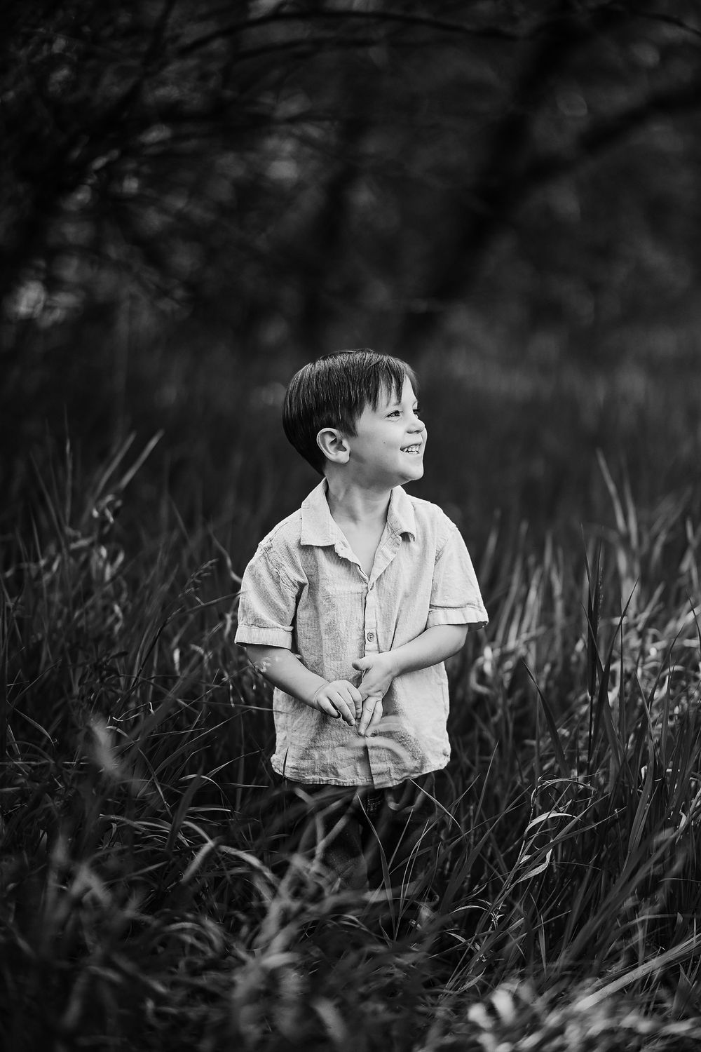 Black and white photo of a child sitting in tall grass looking to the side in natural light.