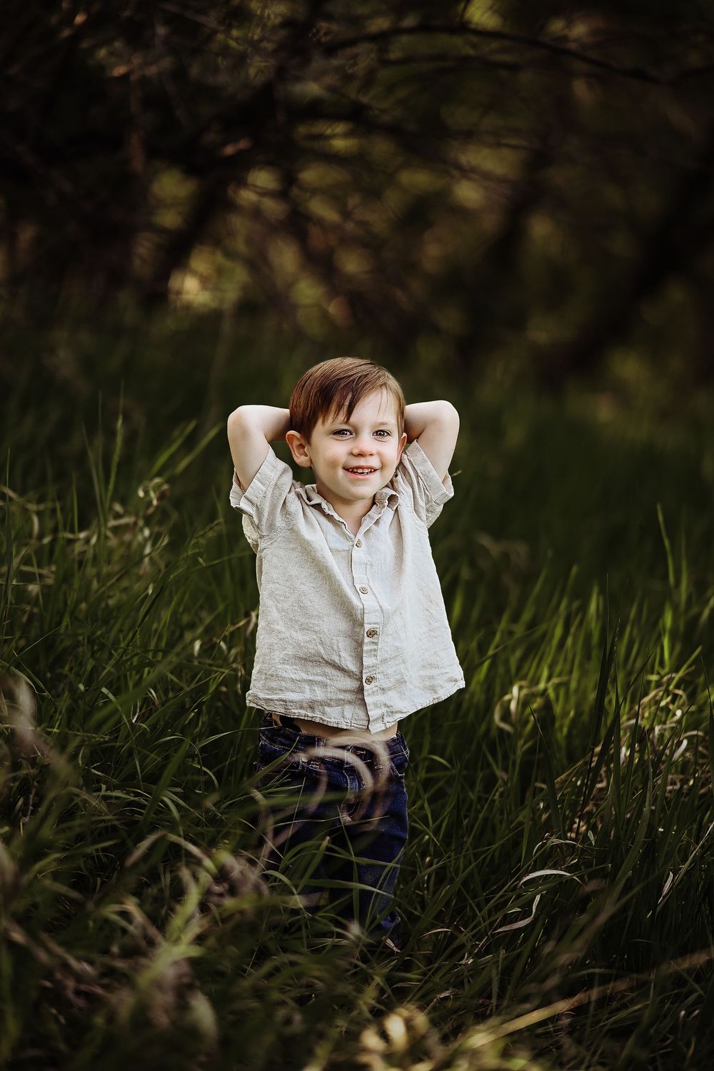 A child plays joyfully in tall grass during a sunny outdoor photo session.