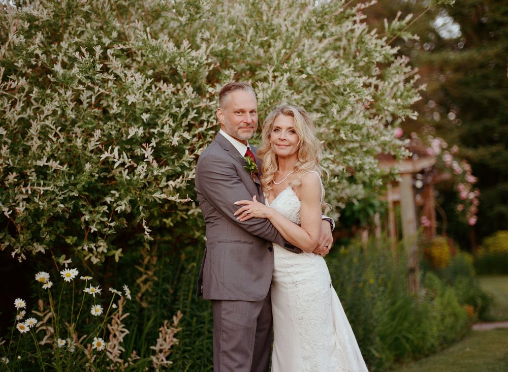 Romantic bride and groom sharing intimate moments in a garden setting surrounded by blooming foliage.