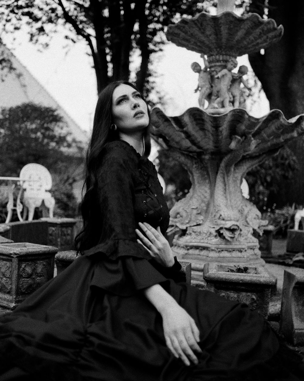 Artistic black and white portrait series showing gothic fashion with dark dress in an outdoor garden setting.
