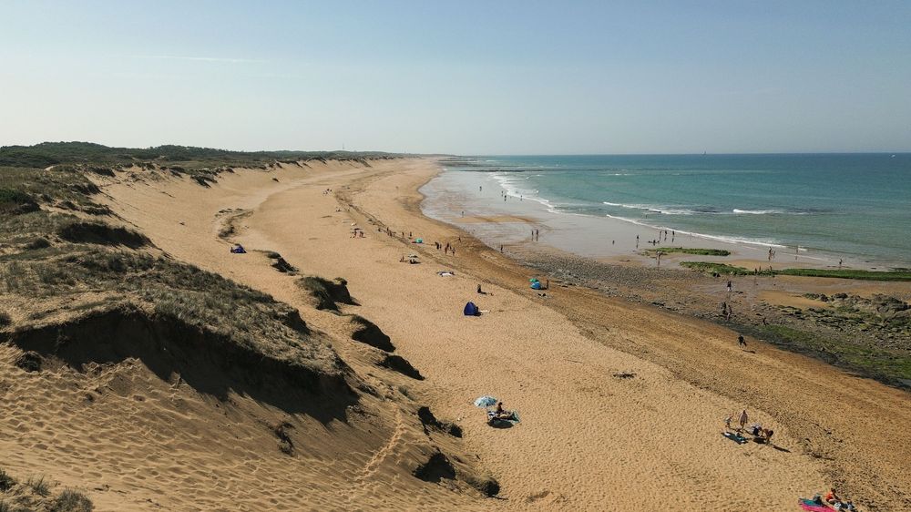 Panoramic view of sandy beach with turquoise ocean waves and coastal sand dunes stretching along the shoreline.