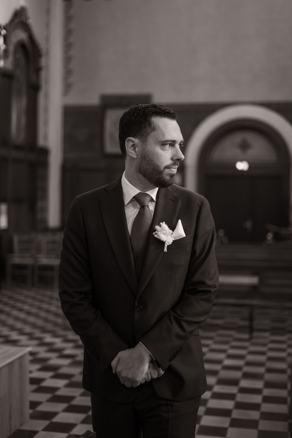 Black and white photo series showing a man in a formal suit with white boutonniere leaning over against a checkered floor.