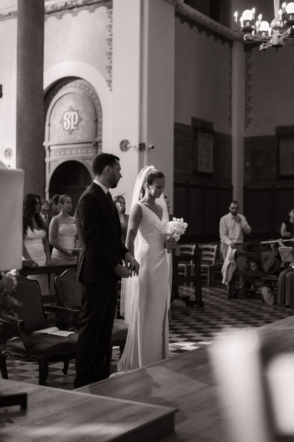 Black and white wedding ceremony photos show guests and couple in a room with checkered floor and columns.