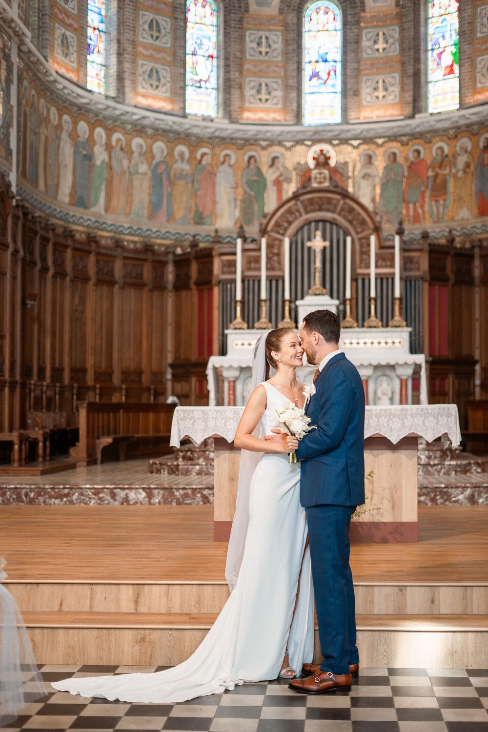 A wedding couple shares intimate moments in a grand church with ornate architecture and stained glass windows.