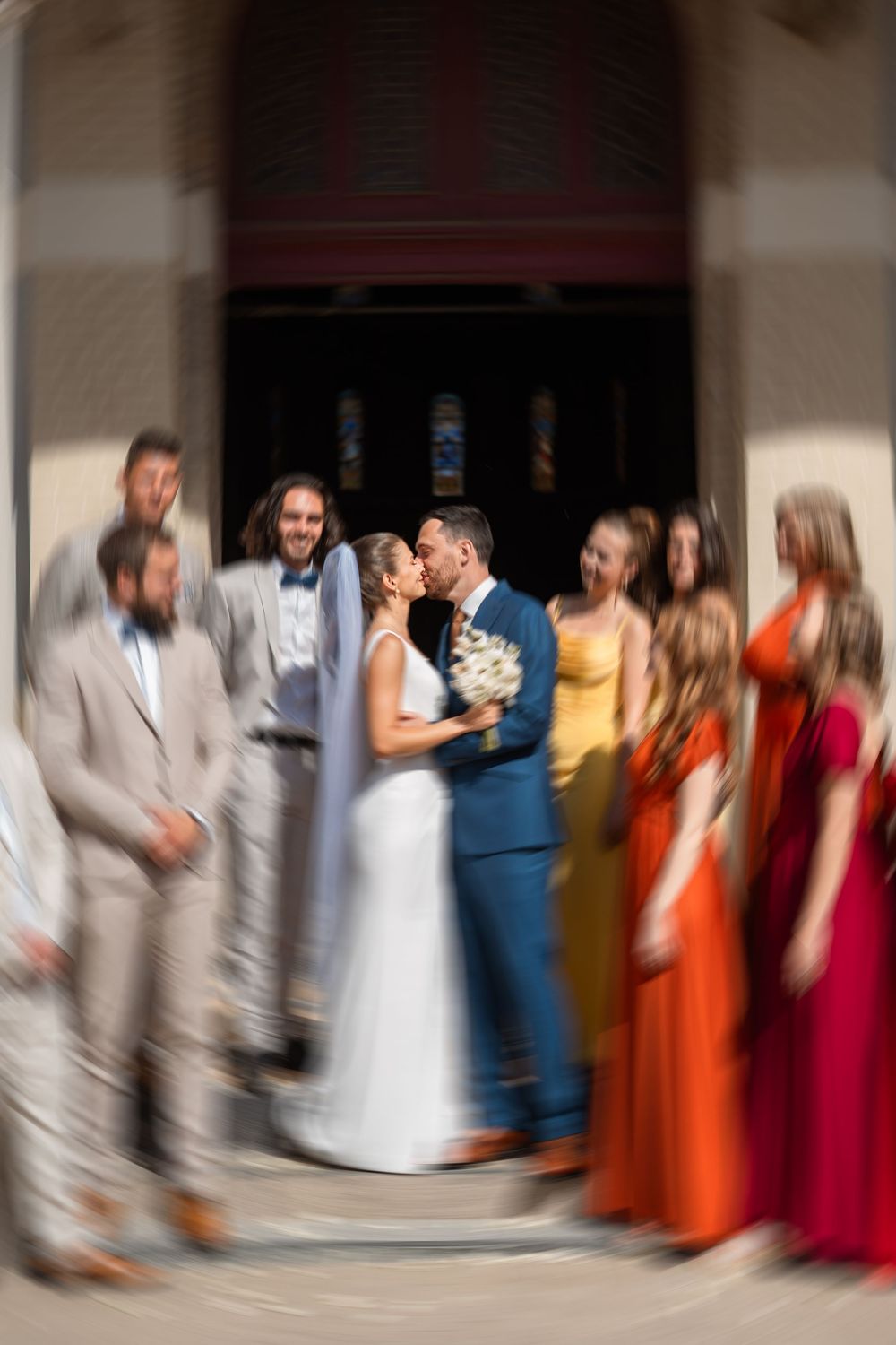Motion blur captures a wedding party lineup in formal attire including colorful dresses and suits in an indoor setting.