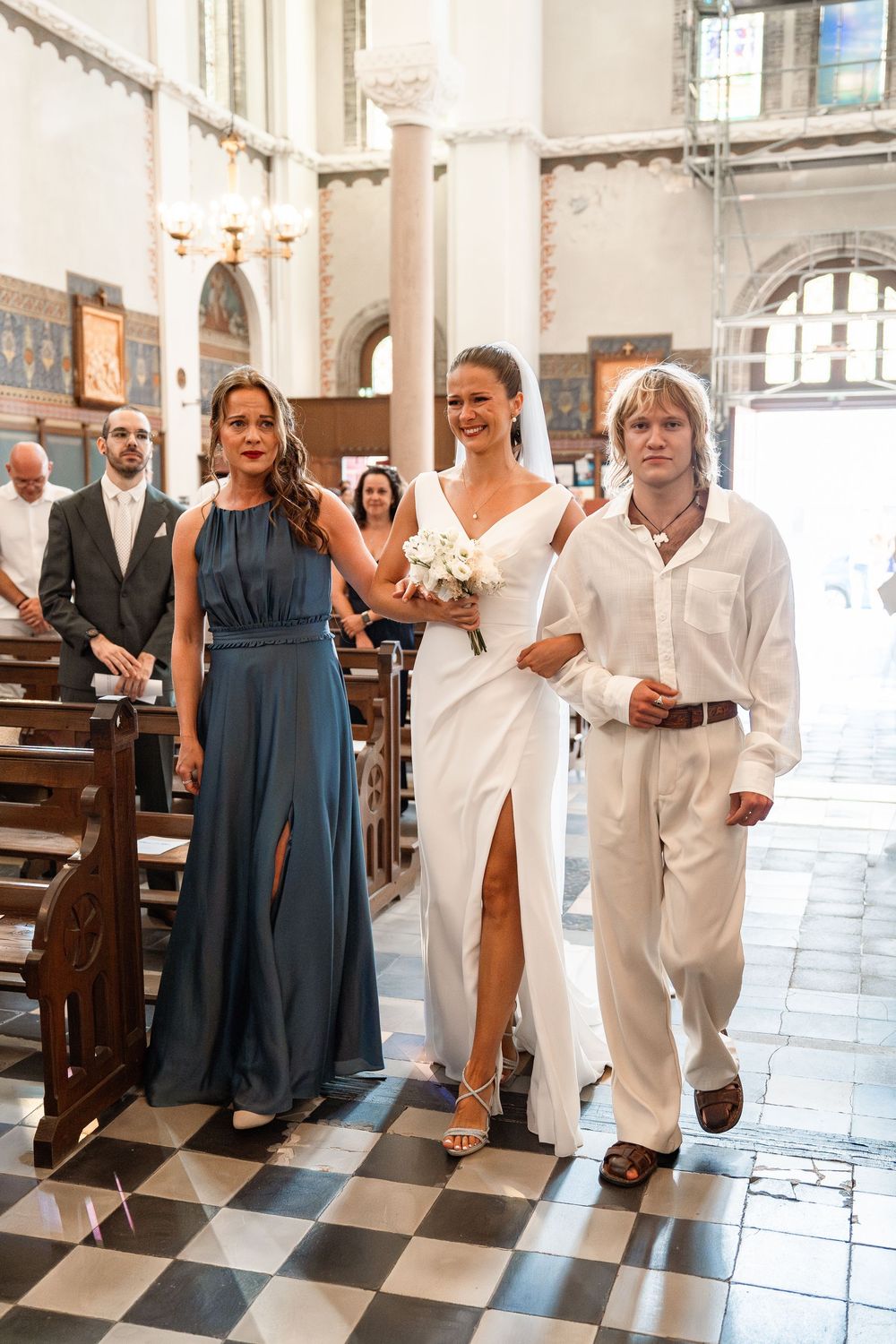 Wedding party poses playfully on black and white checkered floor inside an elegant church.