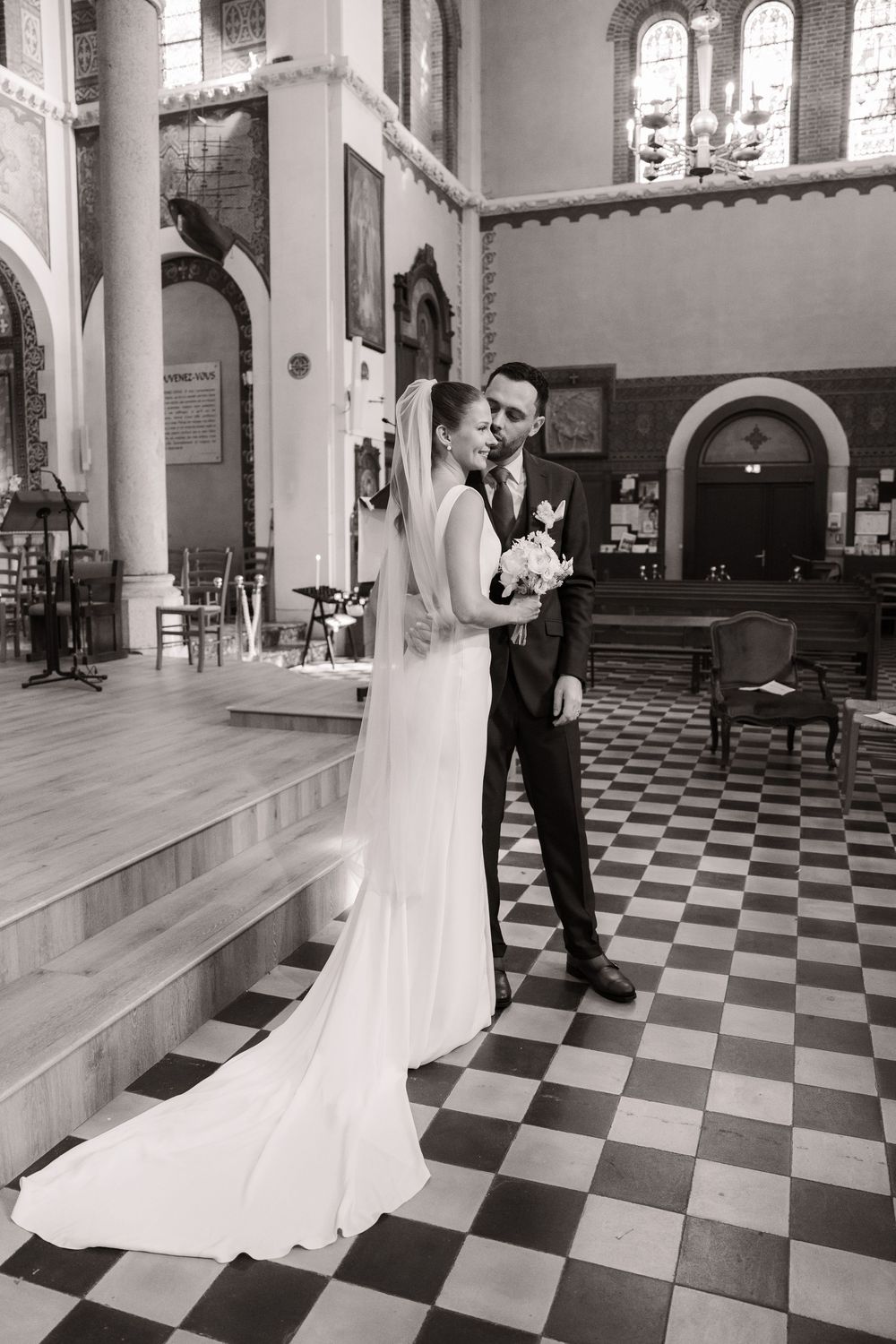 Elegant black and white checkered church floor creates dramatic perspective with flowing white wedding dress and formal attire.