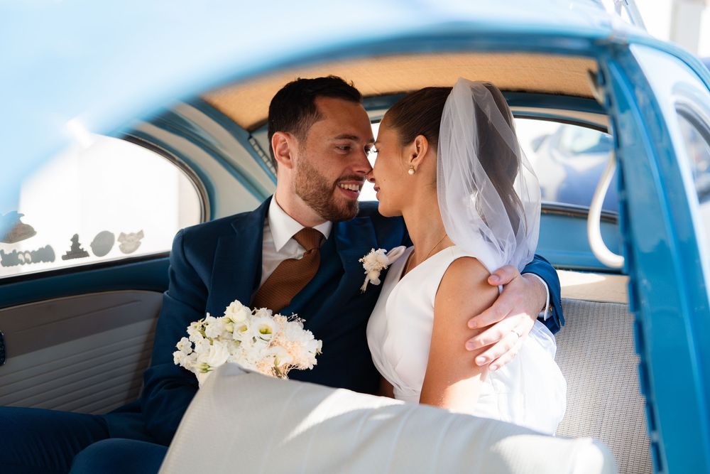 A newlywed couple shares an intimate moment in the backseat of a classic blue vintage car.