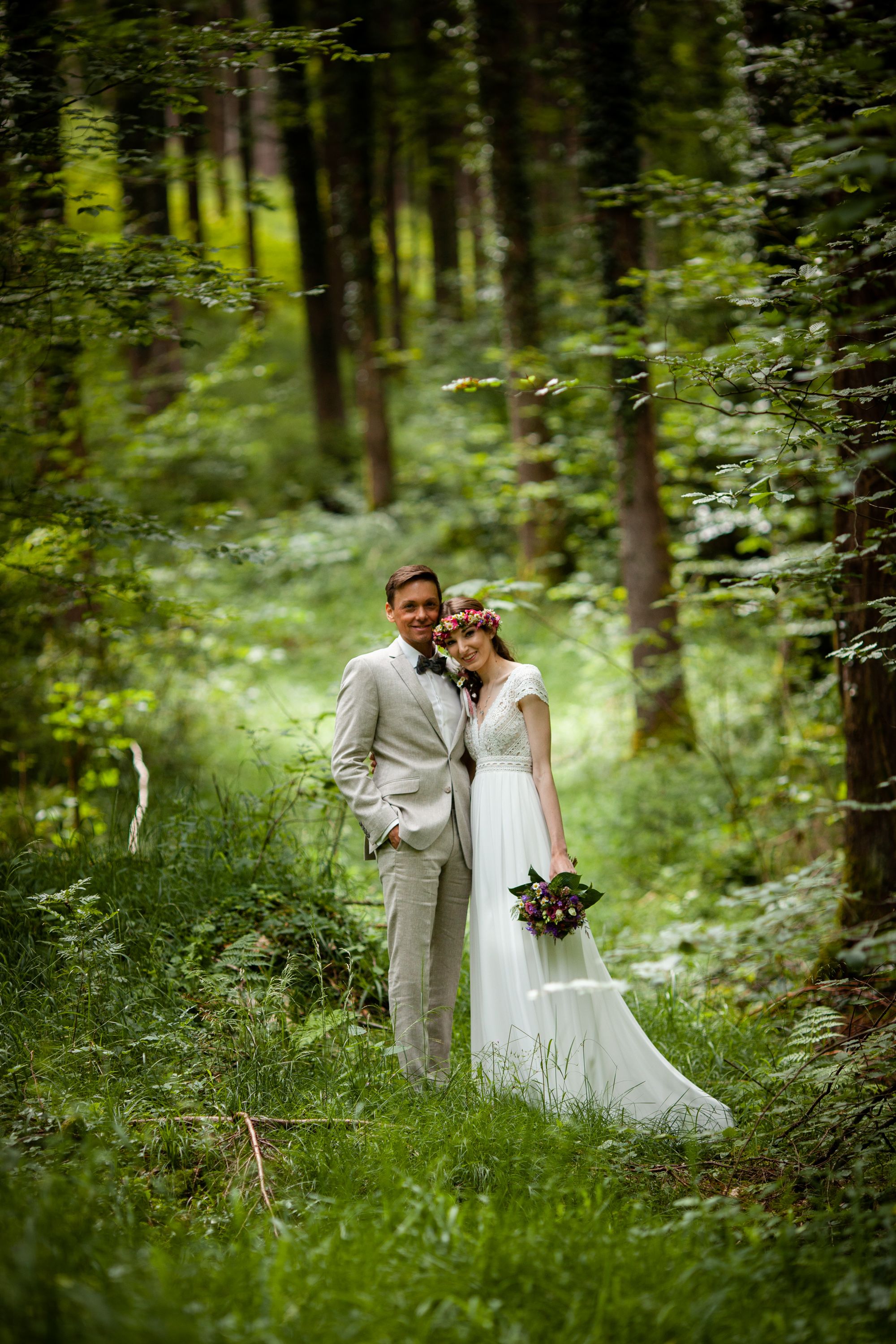 A bride and groom share an intimate moment in a lush green forest setting.