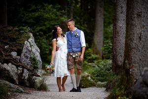 A couple walking hand in hand through a scenic wooded forest path in casual summer attire.