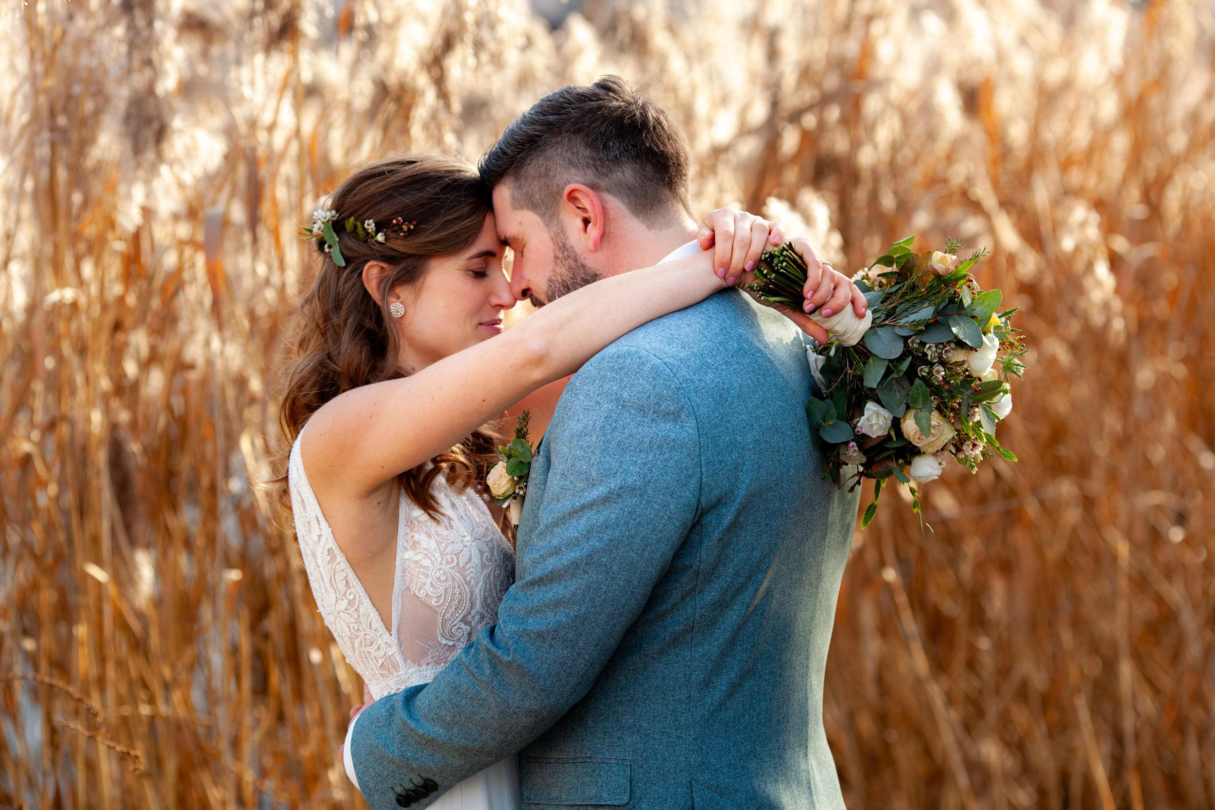 A romantic couple embraces in a golden autumn field during sunset while holding a floral bouquet.