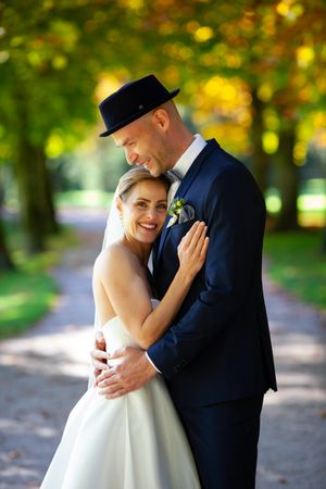 Romantic wedding couple embraces and laughs together on a tree-lined path with golden autumn foliage.