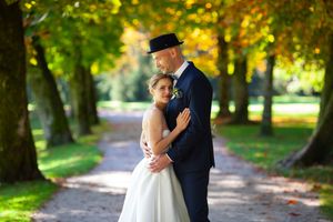 A couple embraces on a tree-lined path during an autumn wedding photoshoot.