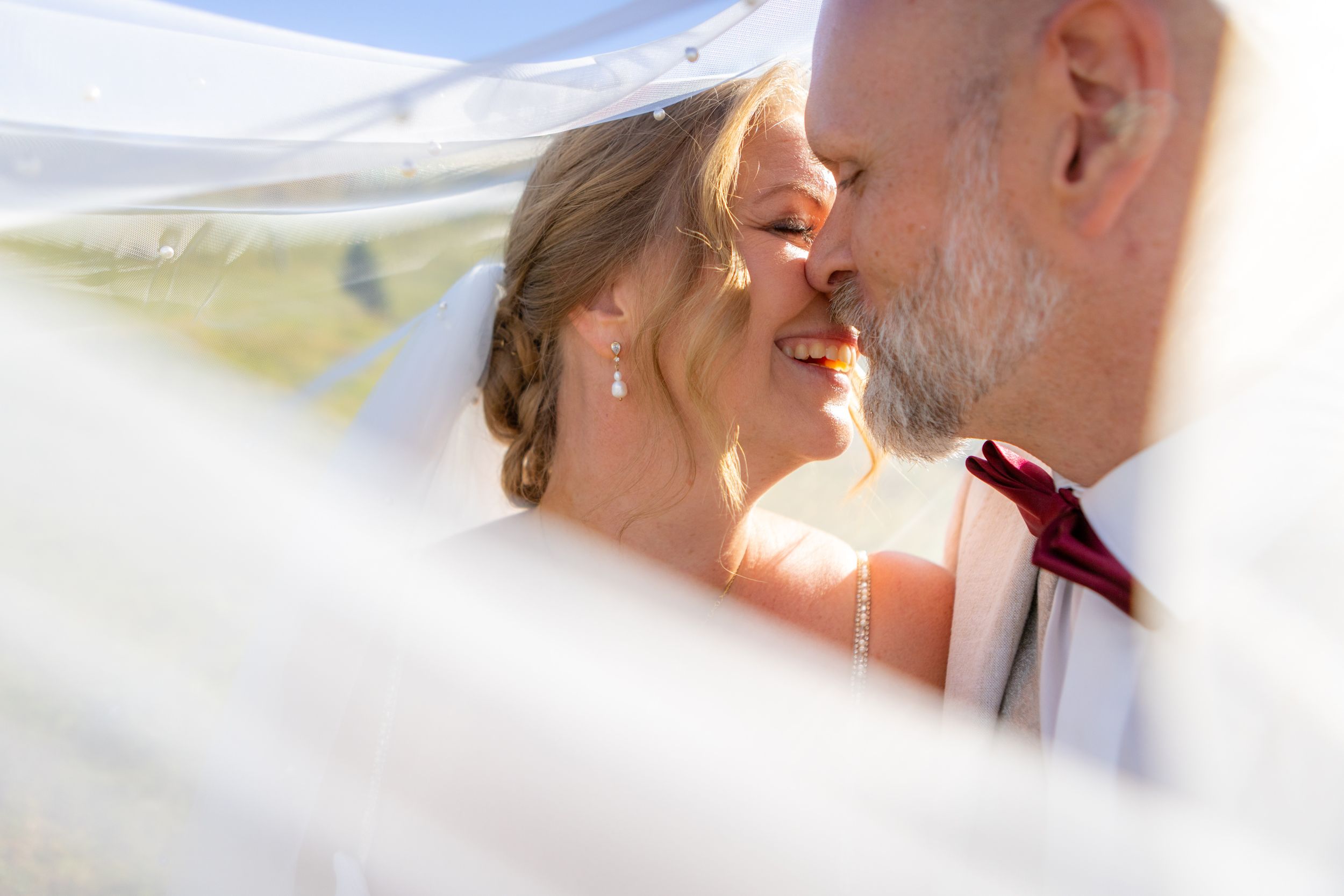 Bride and groom share a romantic kiss under a flowing white veil on their wedding day.