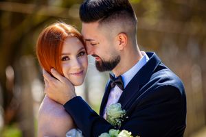 A romantic wedding couple shares an intimate moment outdoors with white flowers and a navy suit.