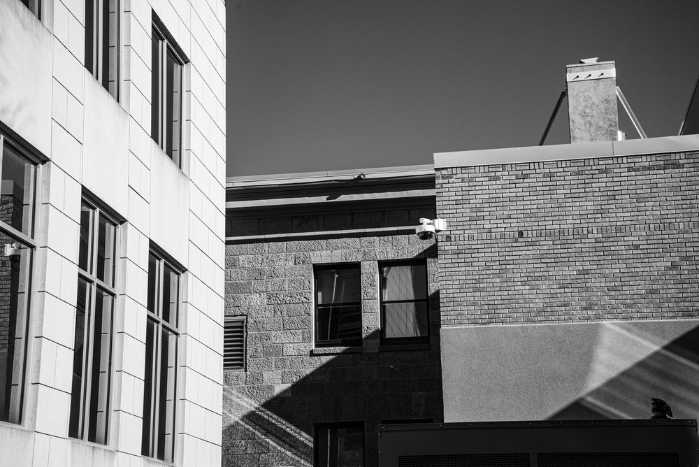 Black and white urban architecture photo showing contrasting brick and stone building facades against a clear sky.