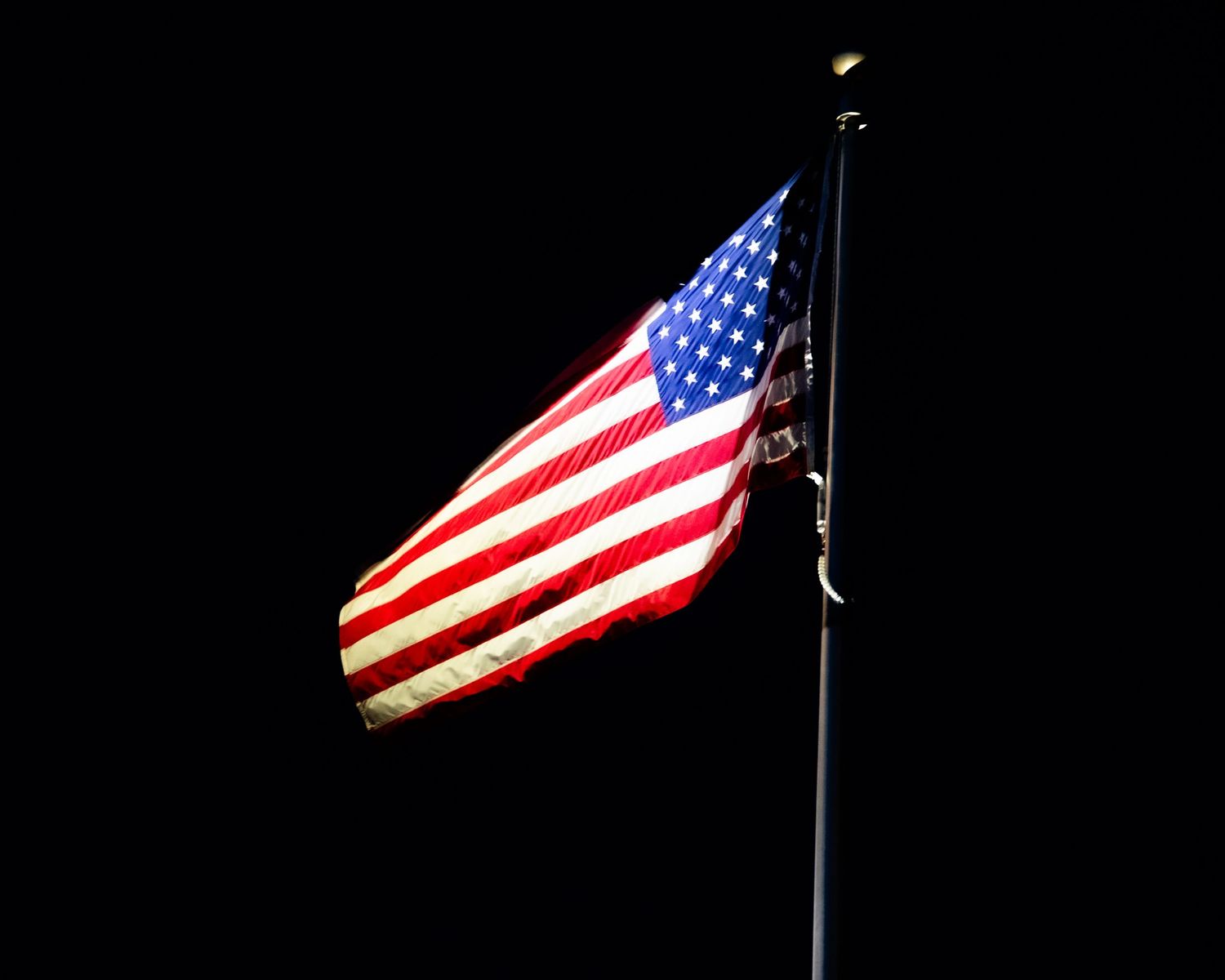 American flag illuminated against a dark night sky, waving proudly on a flagpole.